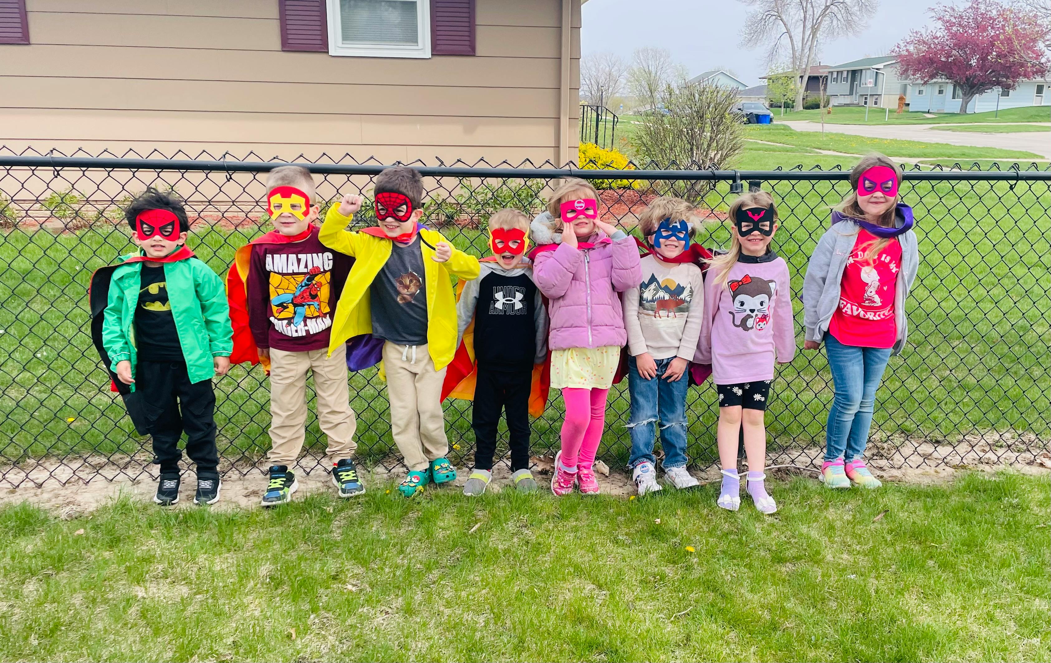 Group of children in superhero costumes and masks standing outdoors