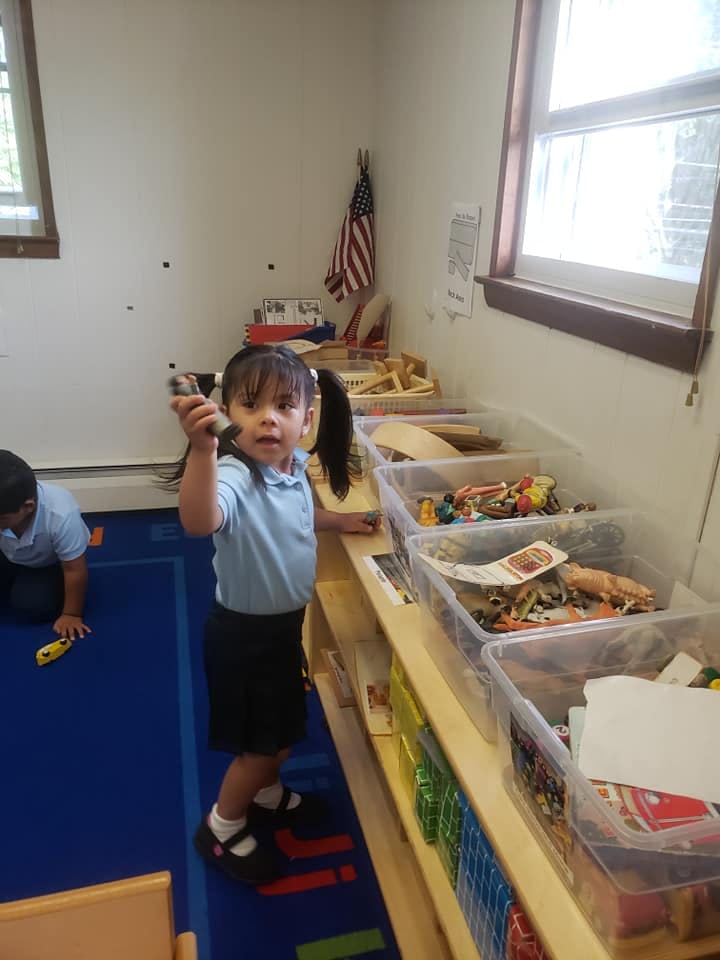 Child holding a toy in a classroom with another child on the floor