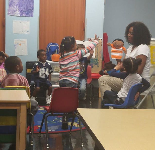 Person with children in a classroom, one child raising a hand