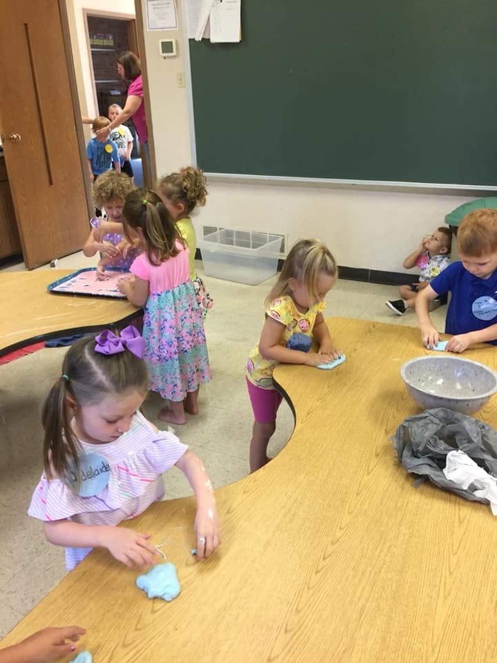 Children playing with blue clay at a table in a classroom