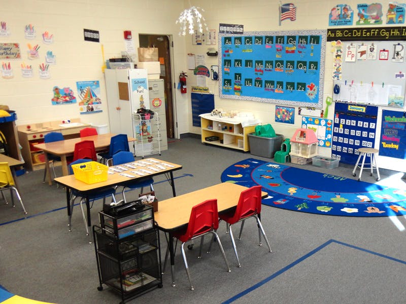 Empty classroom with small tables and chairs, and a blue rug