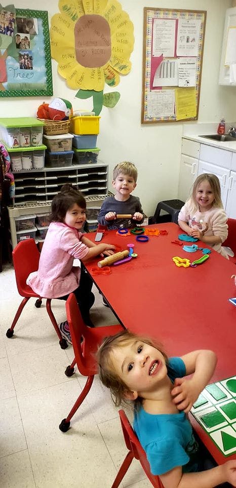 Four children sitting at a red table with playdough and toys