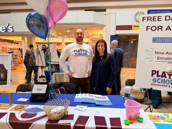 Two people standing behind a table with balloons at a fair or market