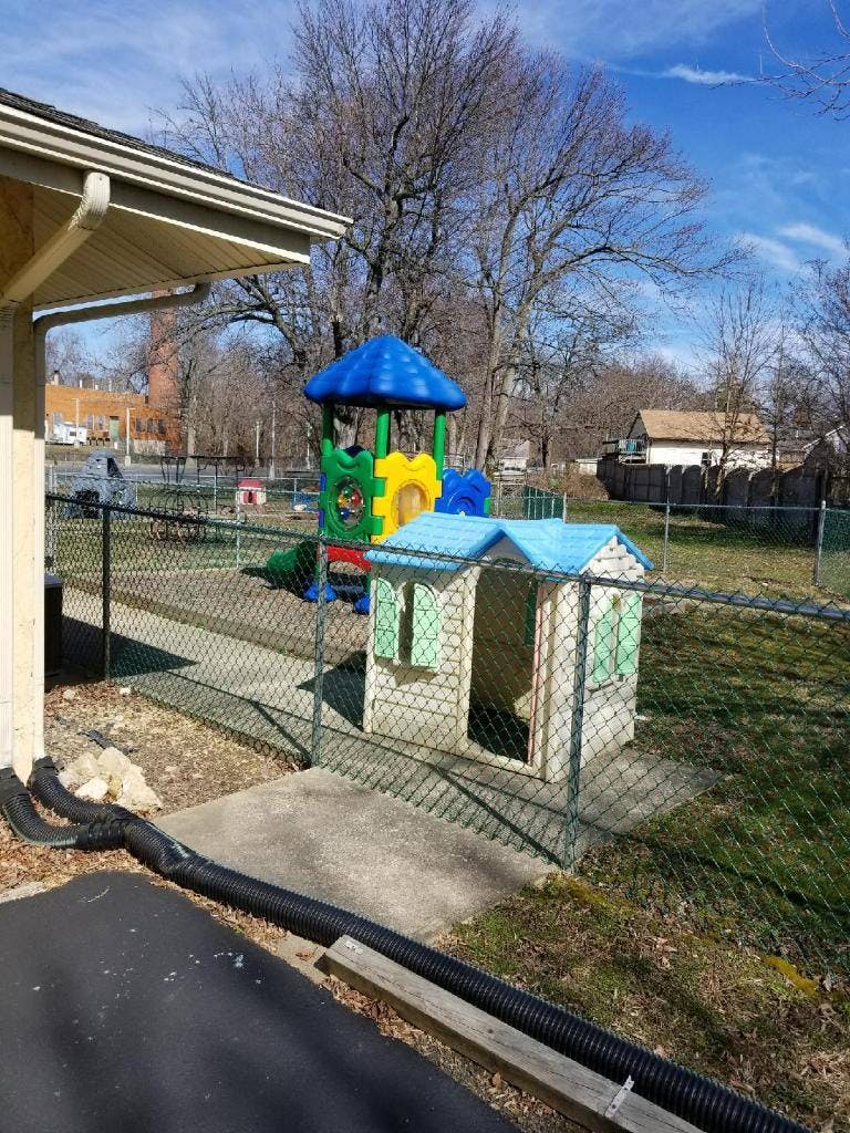 Playground with a colorful play structure and a small playhouse behind a fence