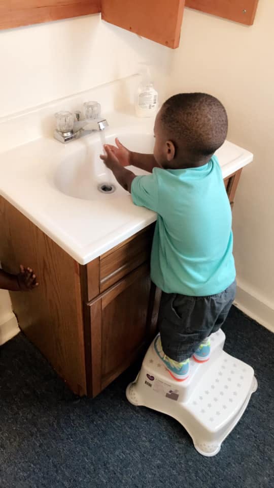 Child standing on a step stool washing hands at a sink