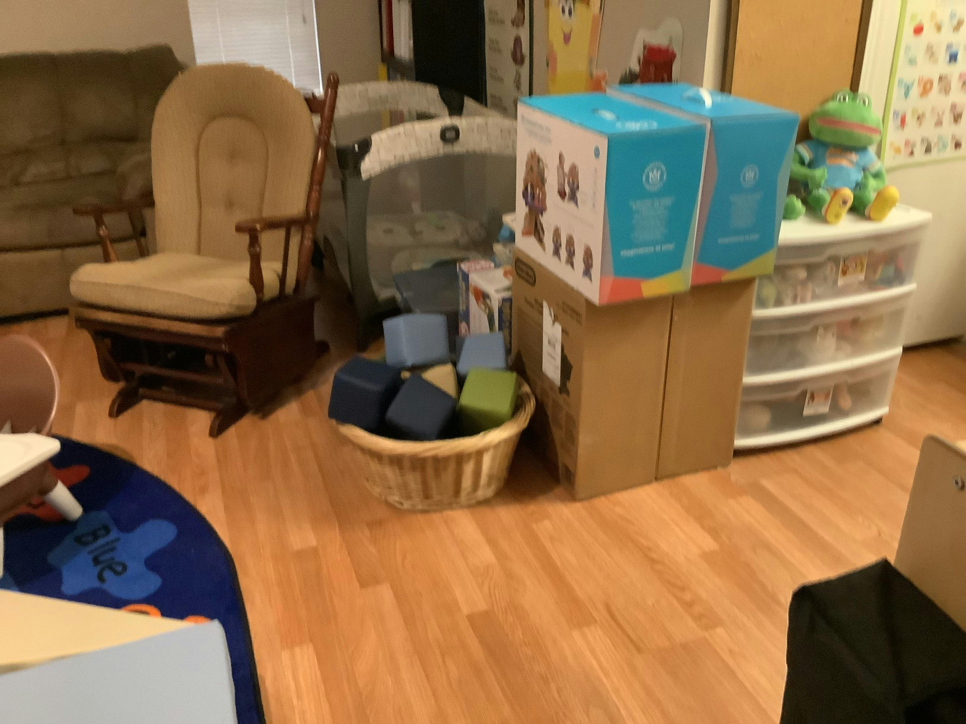 Room with a rocking chair, playpen, boxes, and a basket of blocks