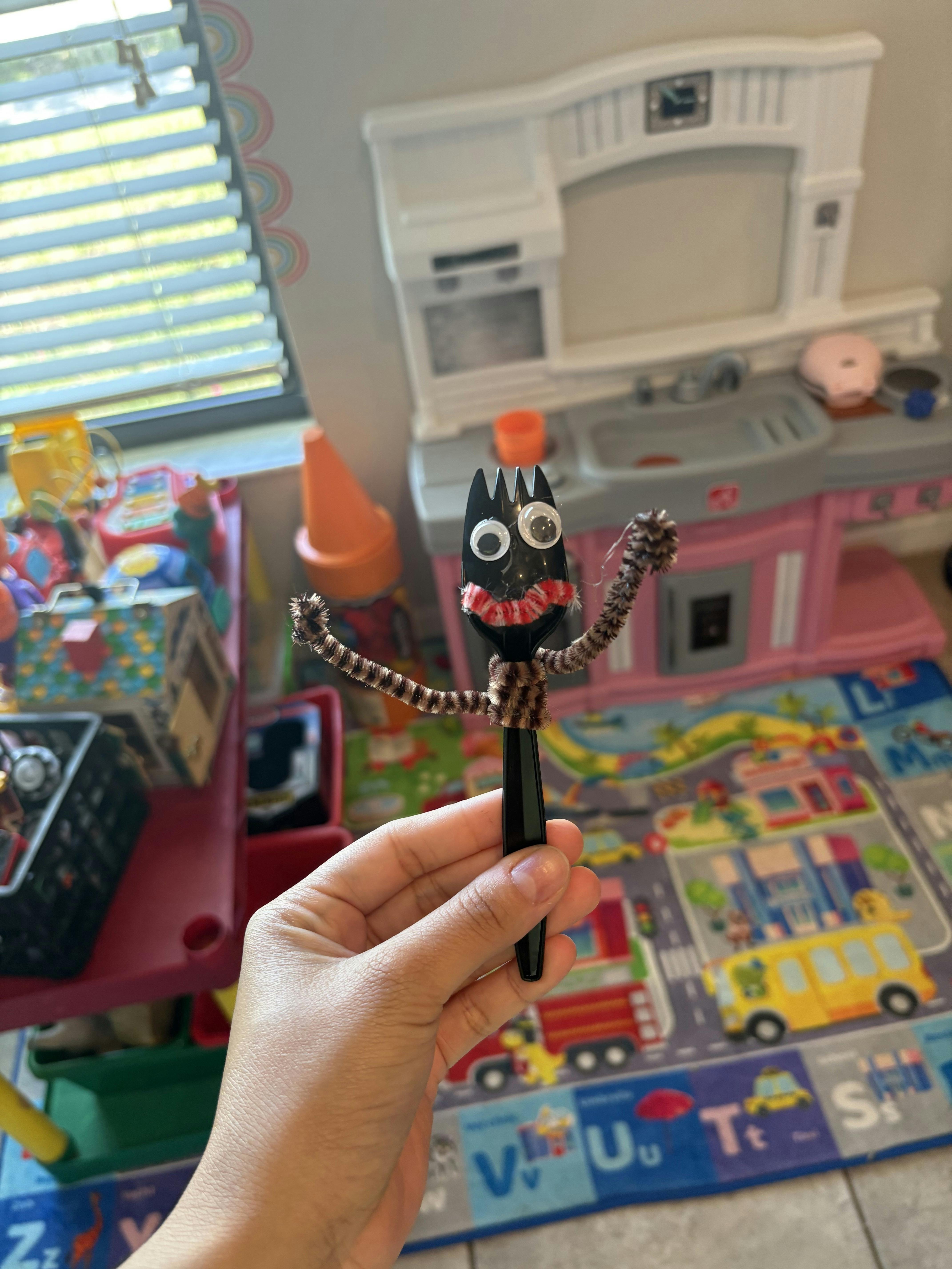 A person's hand holding a plastic fork decorated with googly eyes and pipe cleaners
