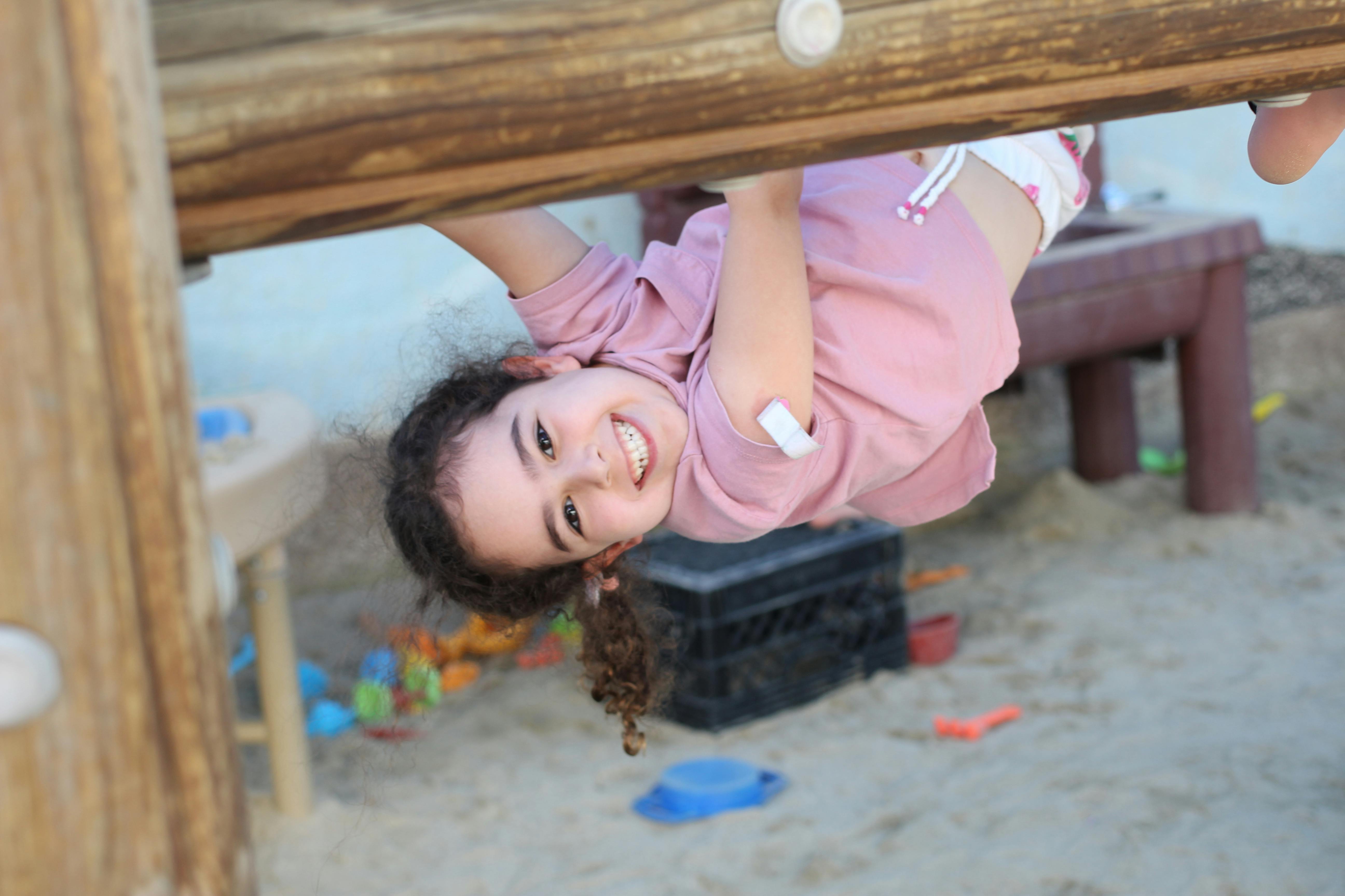 Child hanging upside down from a wooden beam