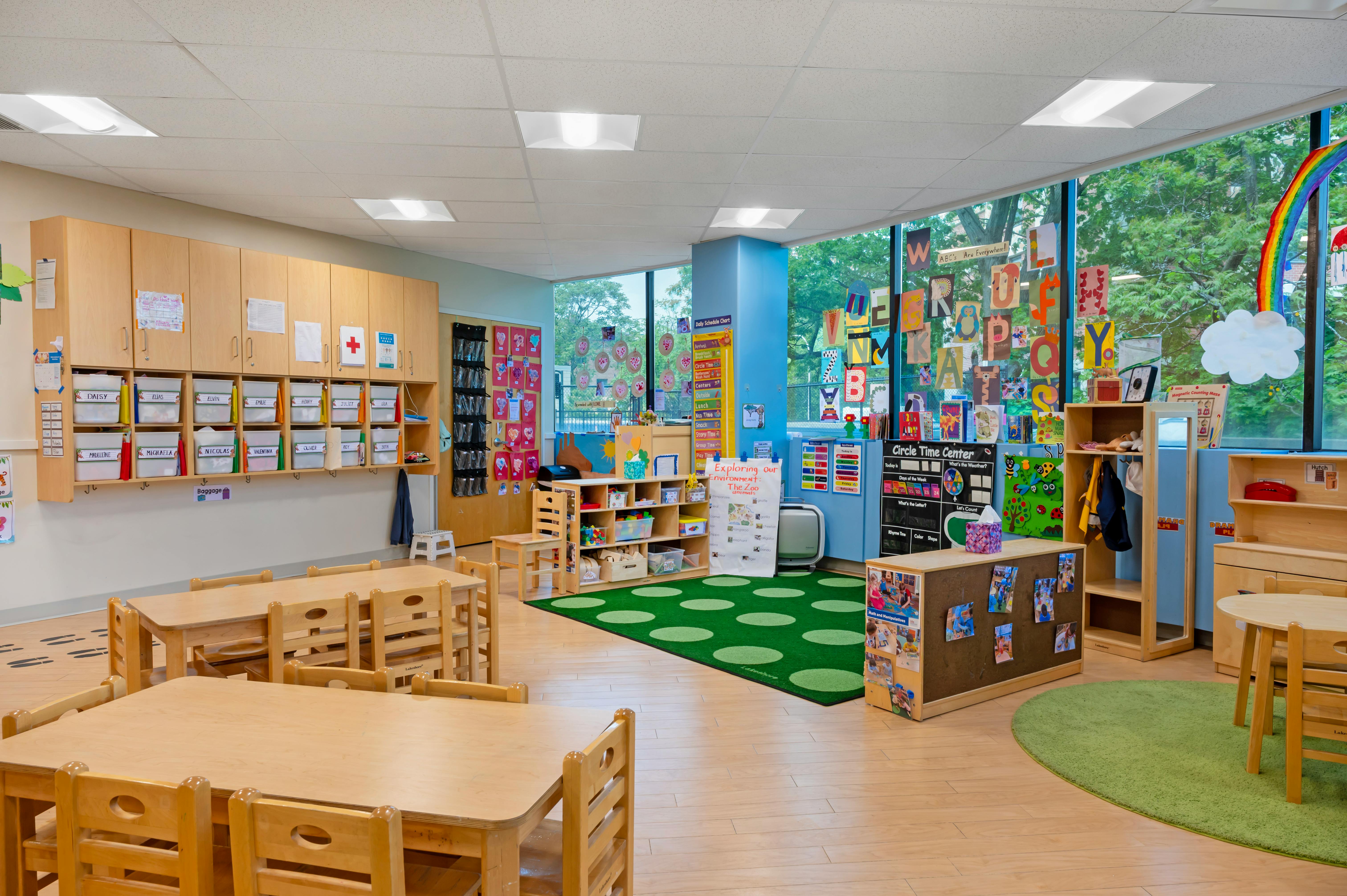 Empty preschool classroom with small wooden tables and chairs on rugs