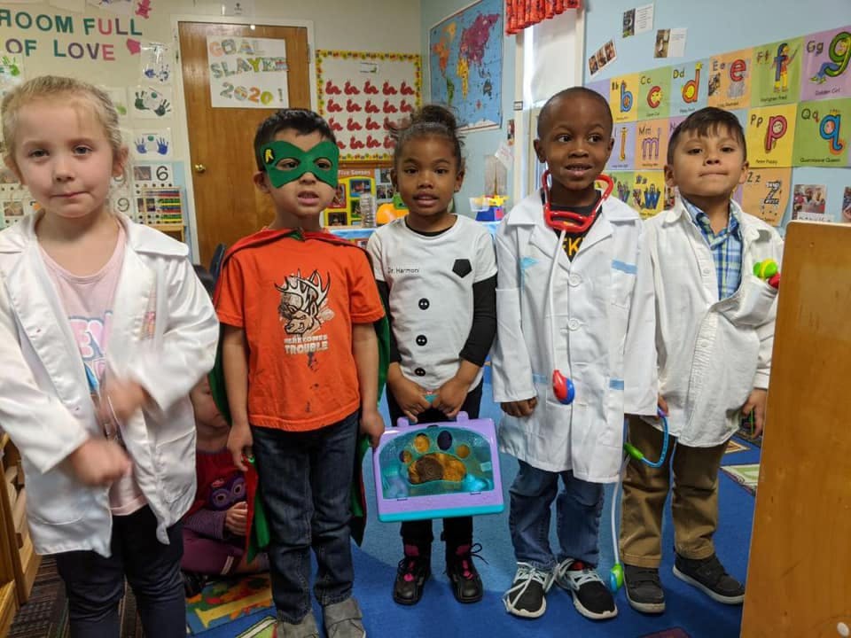 Five children in a classroom, some wearing doctor coats or costumes