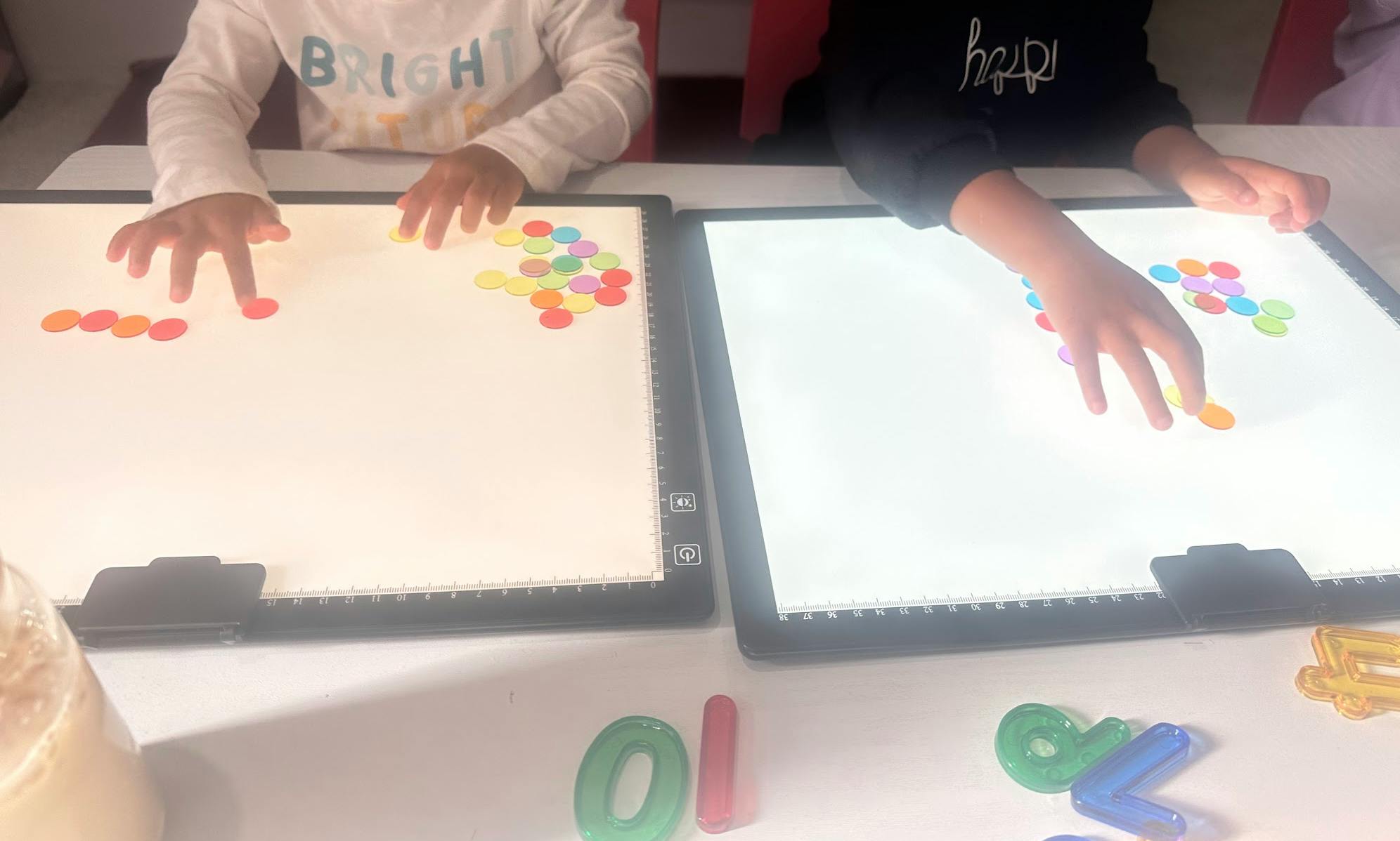 Two children playing with colorful counting discs on light boxes