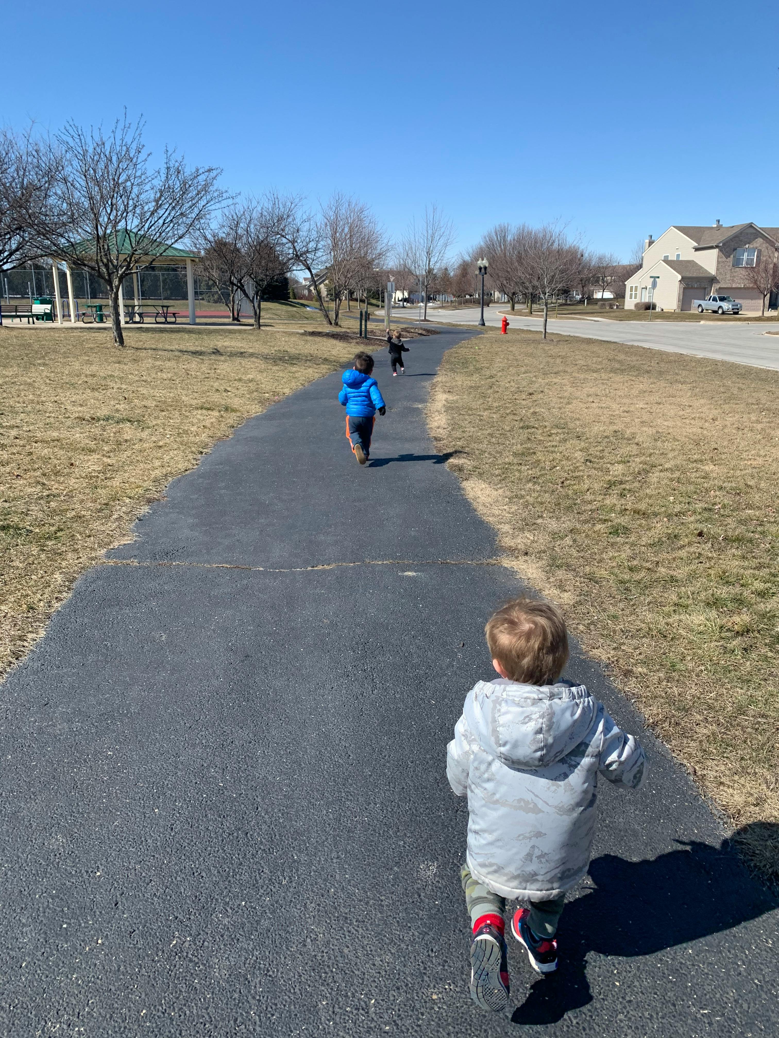Three children running on a paved path outdoors