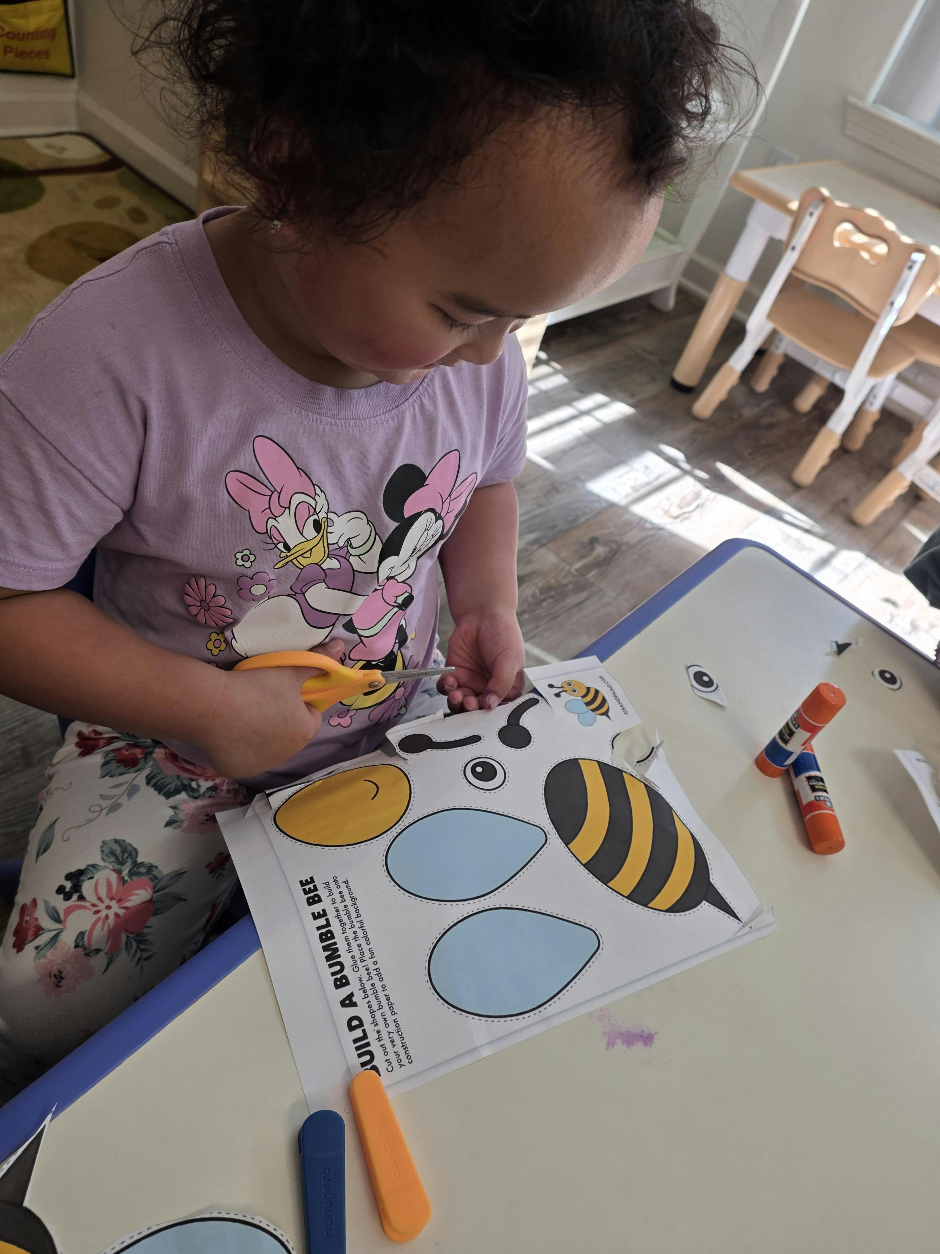 Child cutting out a paper bumblebee craft with scissors