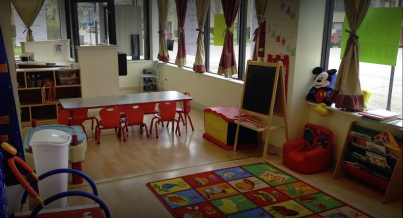 Playroom with small red table and chairs, colorful rug, and easel