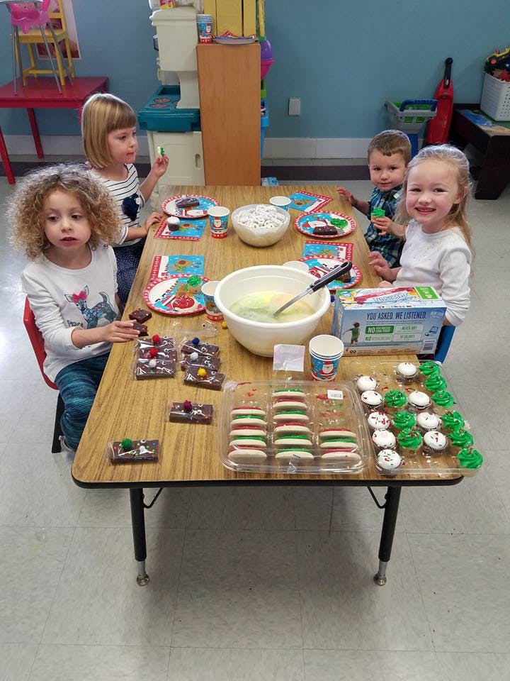 Four children at a table with bowls of frosting and various baked goods