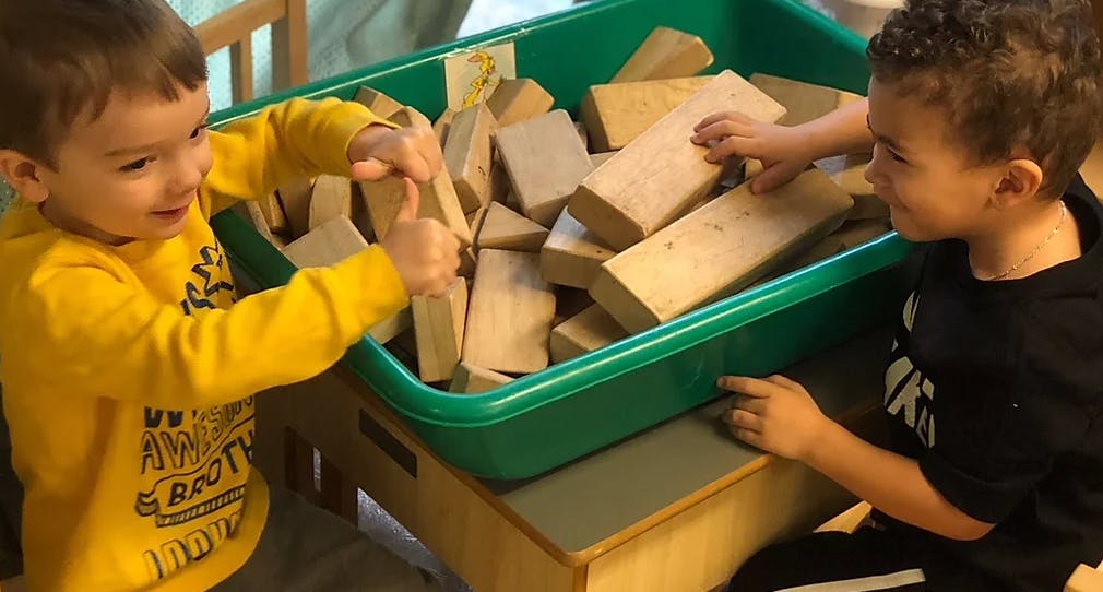 Two children playing with wooden blocks in a green bin