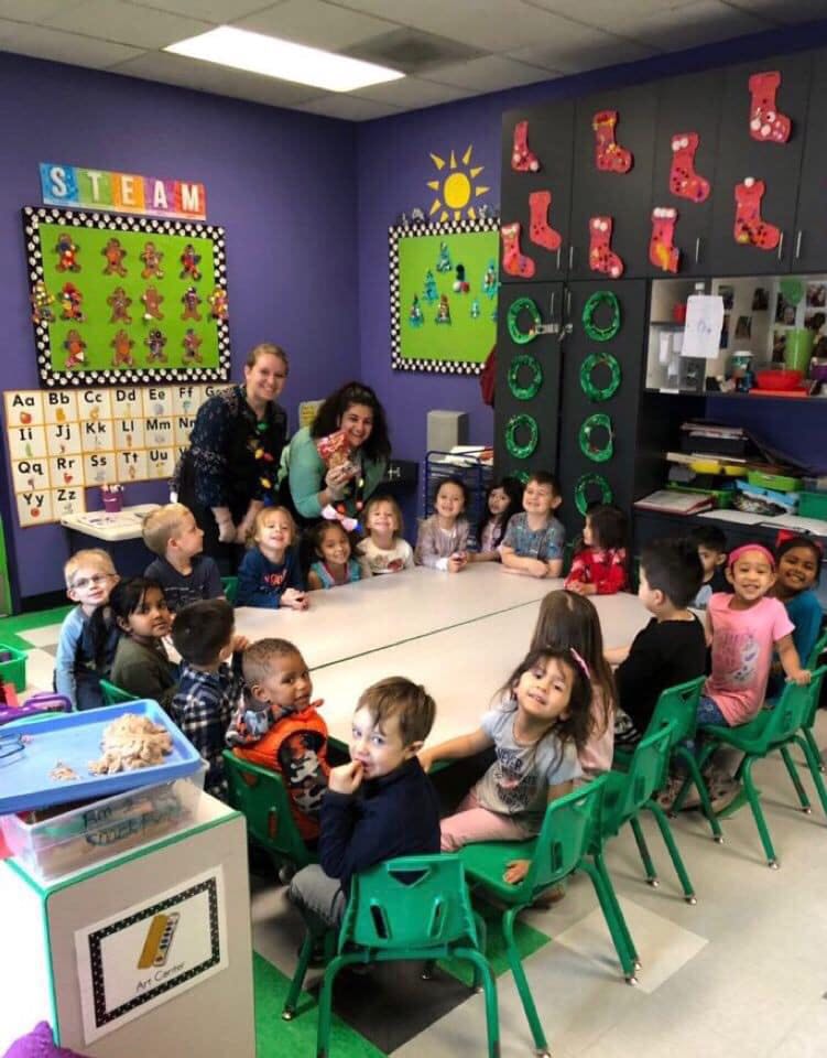 Two adults and multiple children sitting around a table in a classroom