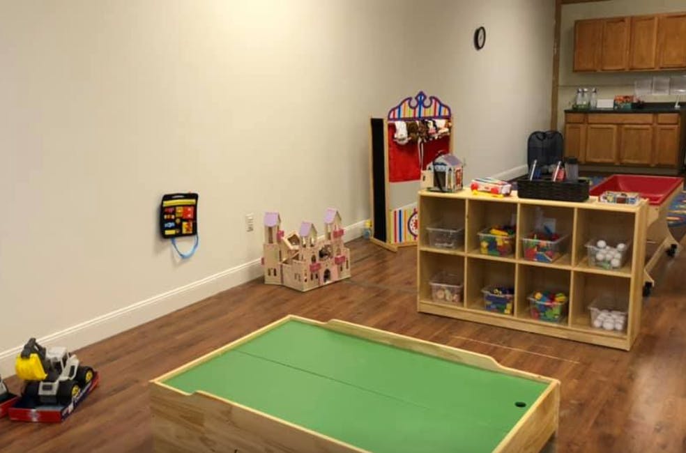 Playroom with toys, including a toy castle, a green play table, and a wooden shelf