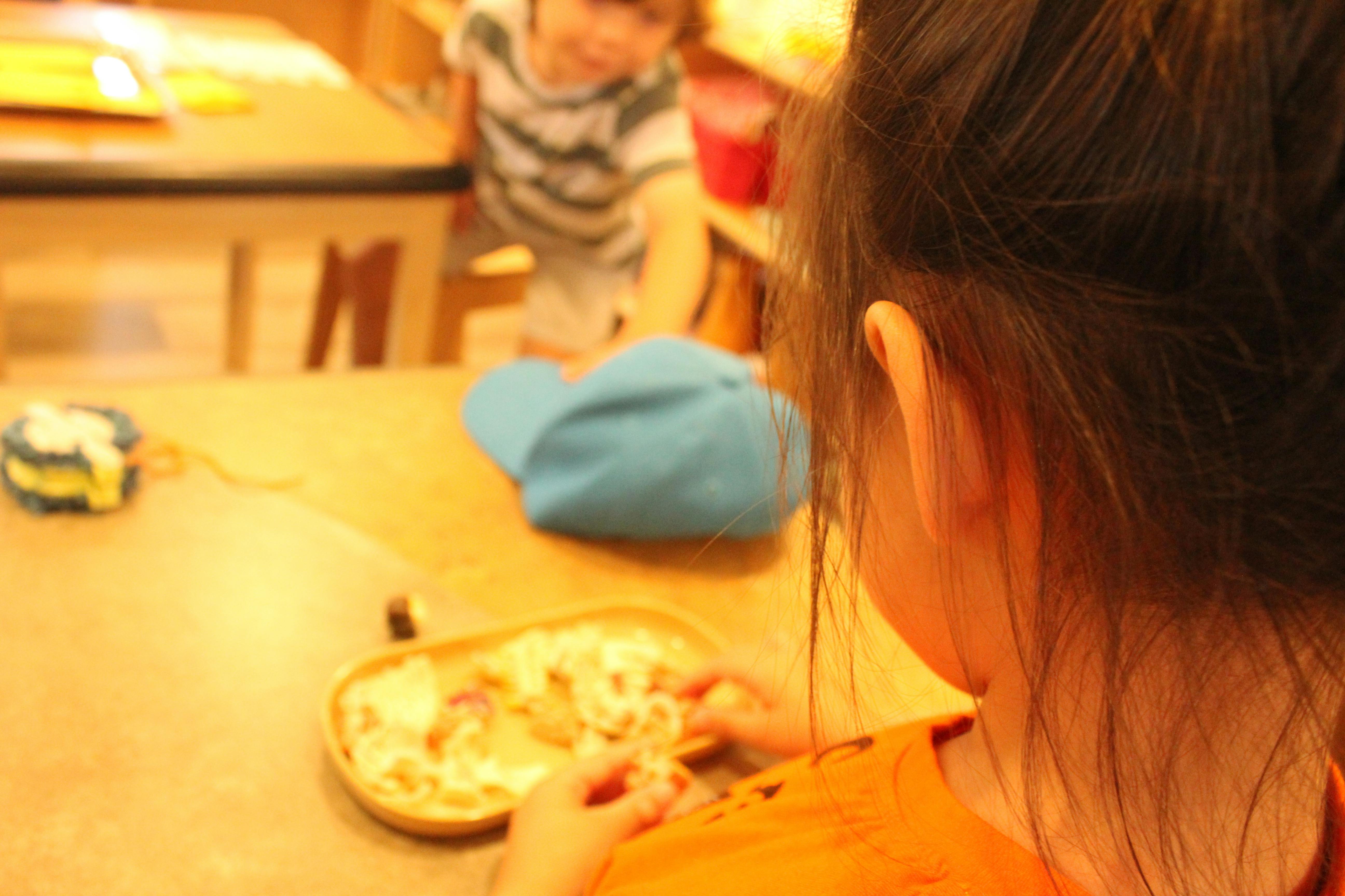 Child eating from a bowl at a table, another child in the background