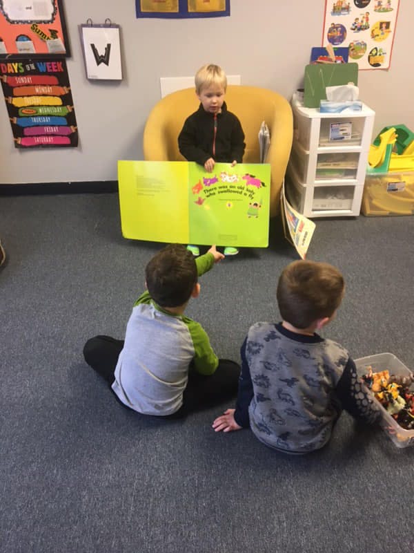 Child in yellow chair reading a book to two children on the floor