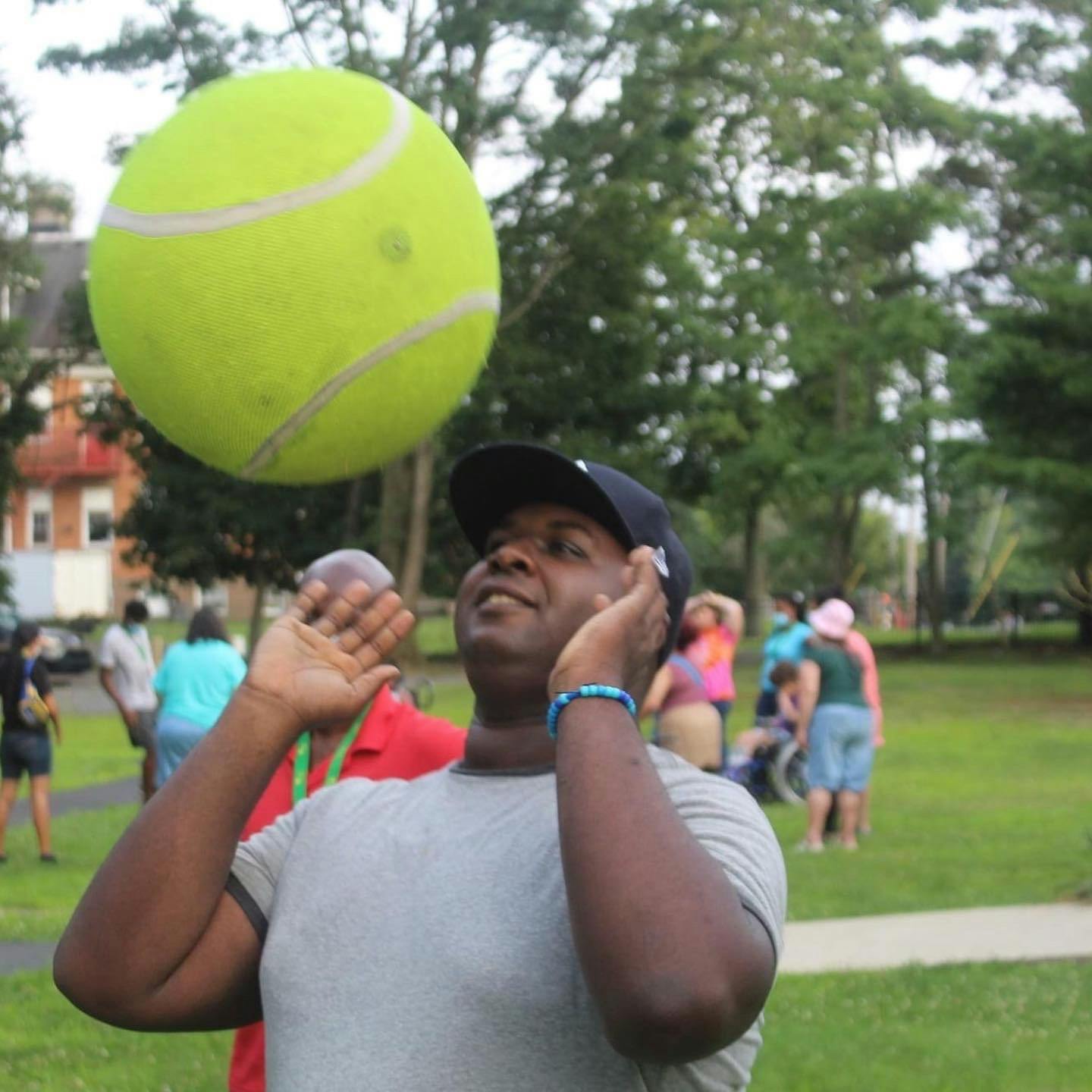 Person in a cap looking up at a large tennis ball in the air