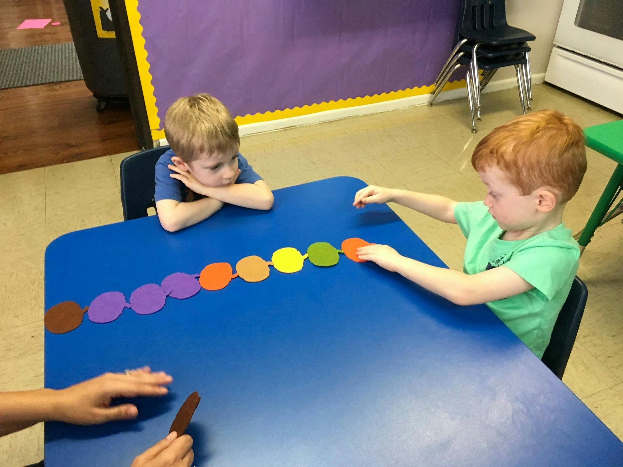 Two children at a table playing with colorful paper circles