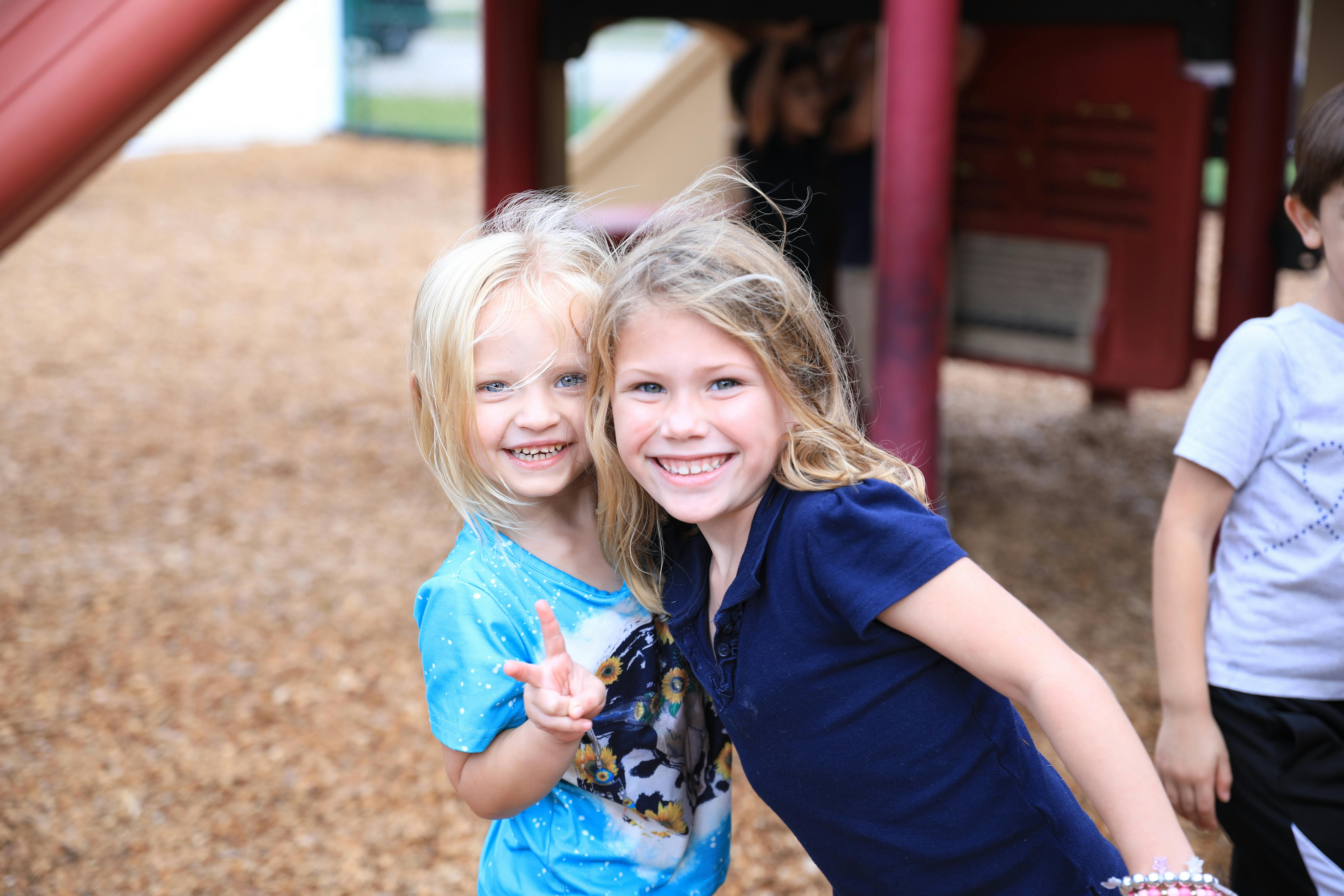 Two children smiling at the camera, one making a peace sign