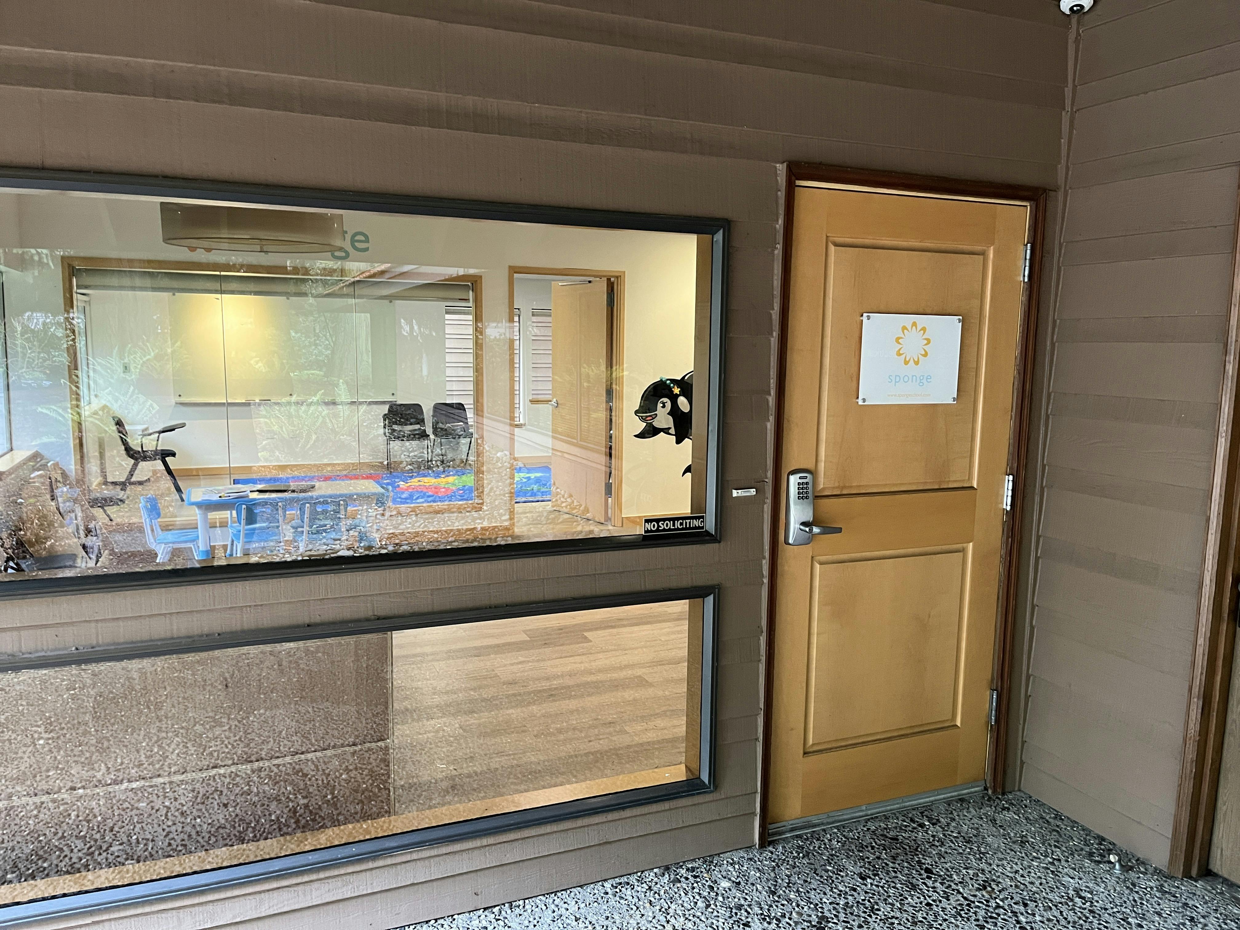 Entrance to a building with a window looking into a classroom and a wooden door with a sign