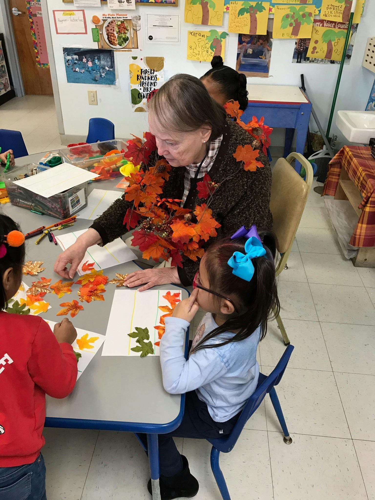 Adult and two children making crafts with leaf cutouts in a classroom
