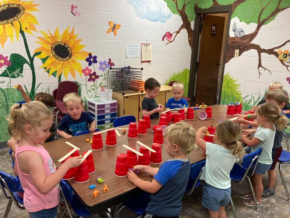 Children at a table playing with red cups and craft sticks