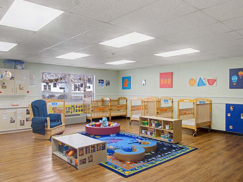 A classroom with cribs, a blue rocking chair, and a play mat