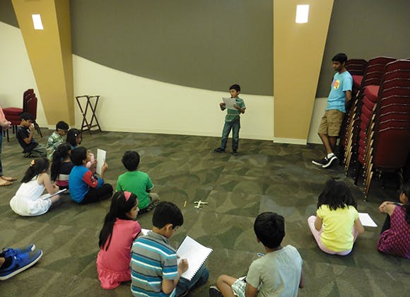 Child standing and reading to other children sitting on the floor