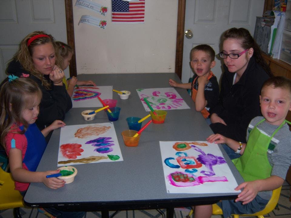 Two people and three children painting at a table