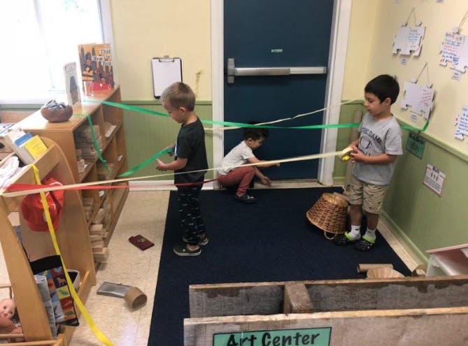 Three children playing with colorful ribbons in a classroom