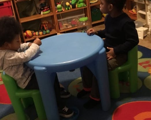 Two children sitting at a small blue table