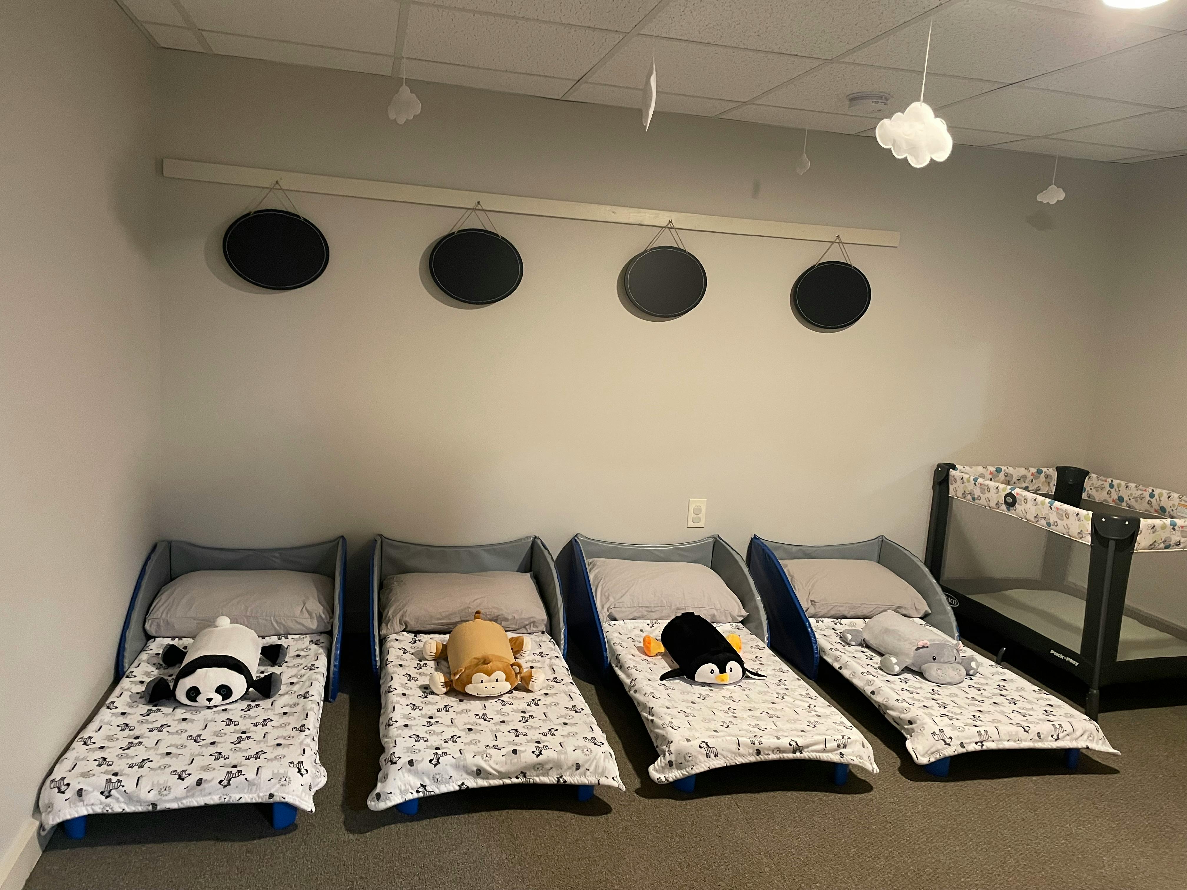 Four toddler beds with stuffed animals and a crib in a room