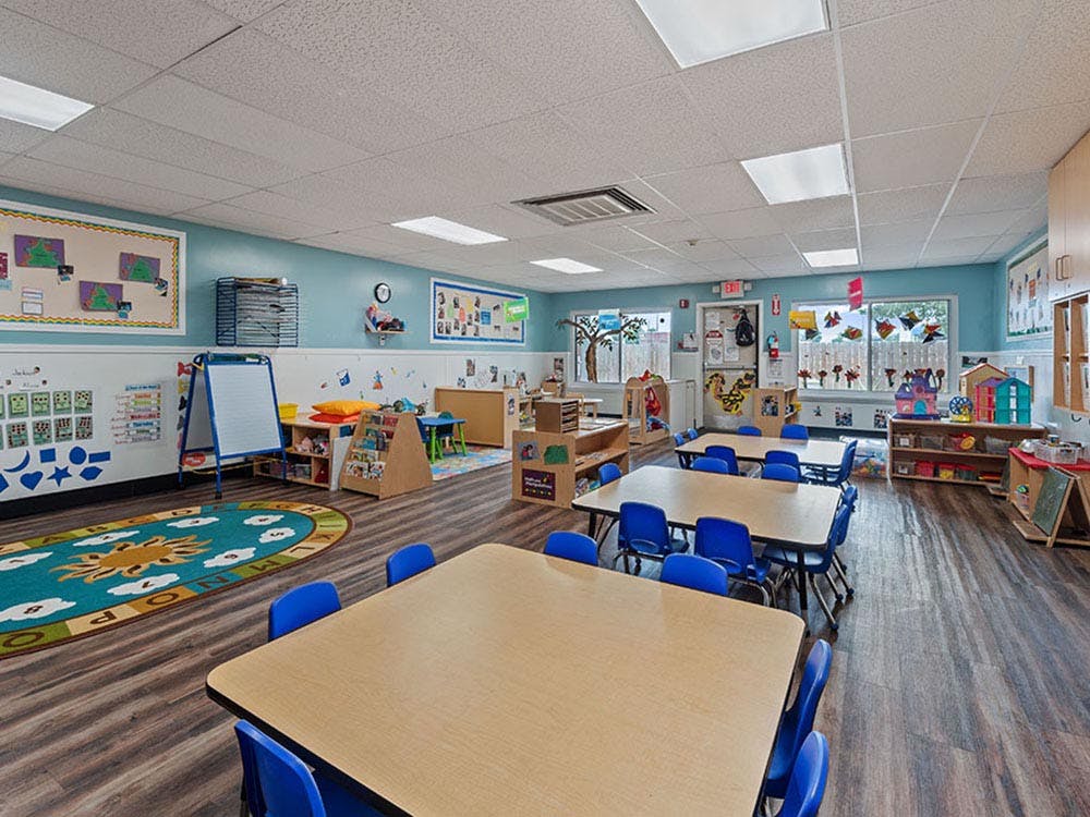 Empty colorful preschool classroom with tables, chairs, and learning materials