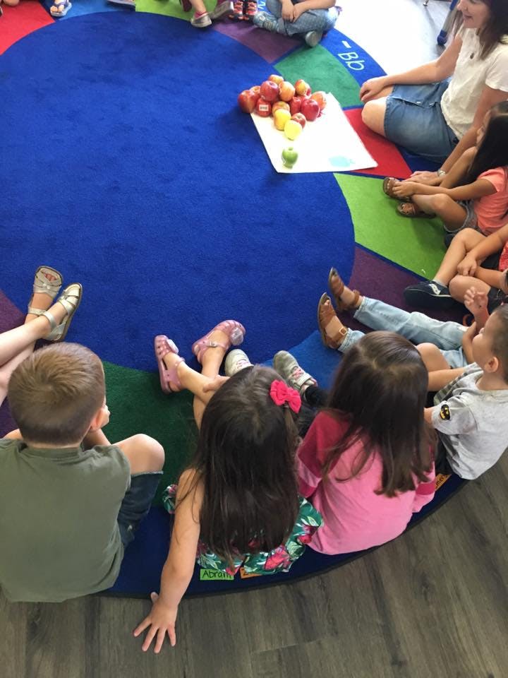 Children sitting on a colorful rug with apples in the center
