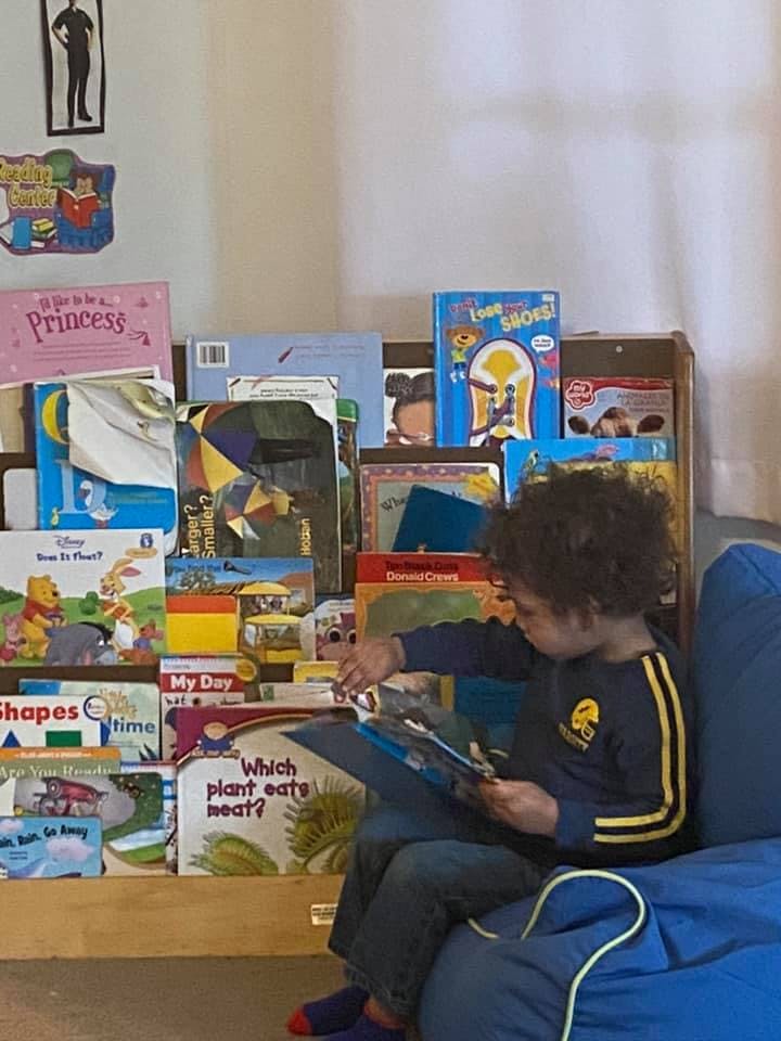 Child sitting on a beanbag chair reading a book next to a bookshelf