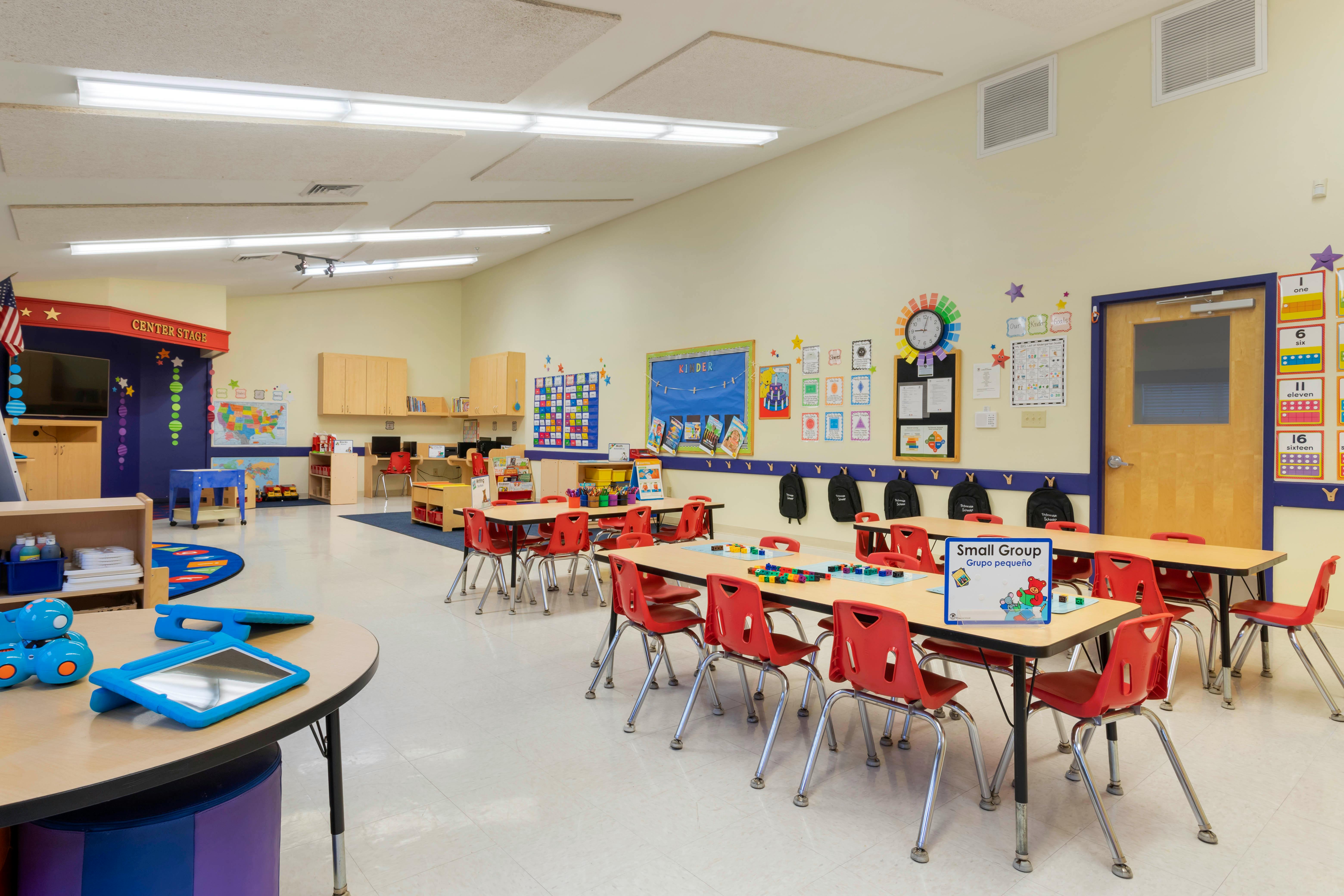 Classroom with small tables and red chairs, computer stations, and colorful decorations