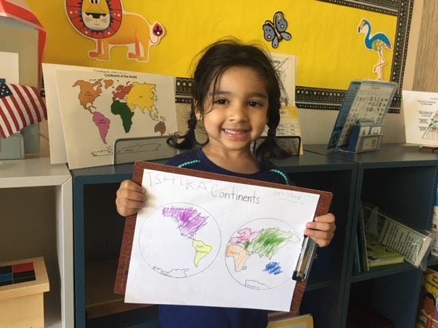 Child holding up a drawing of two world maps with continents colored in color- text reads "Continents"
