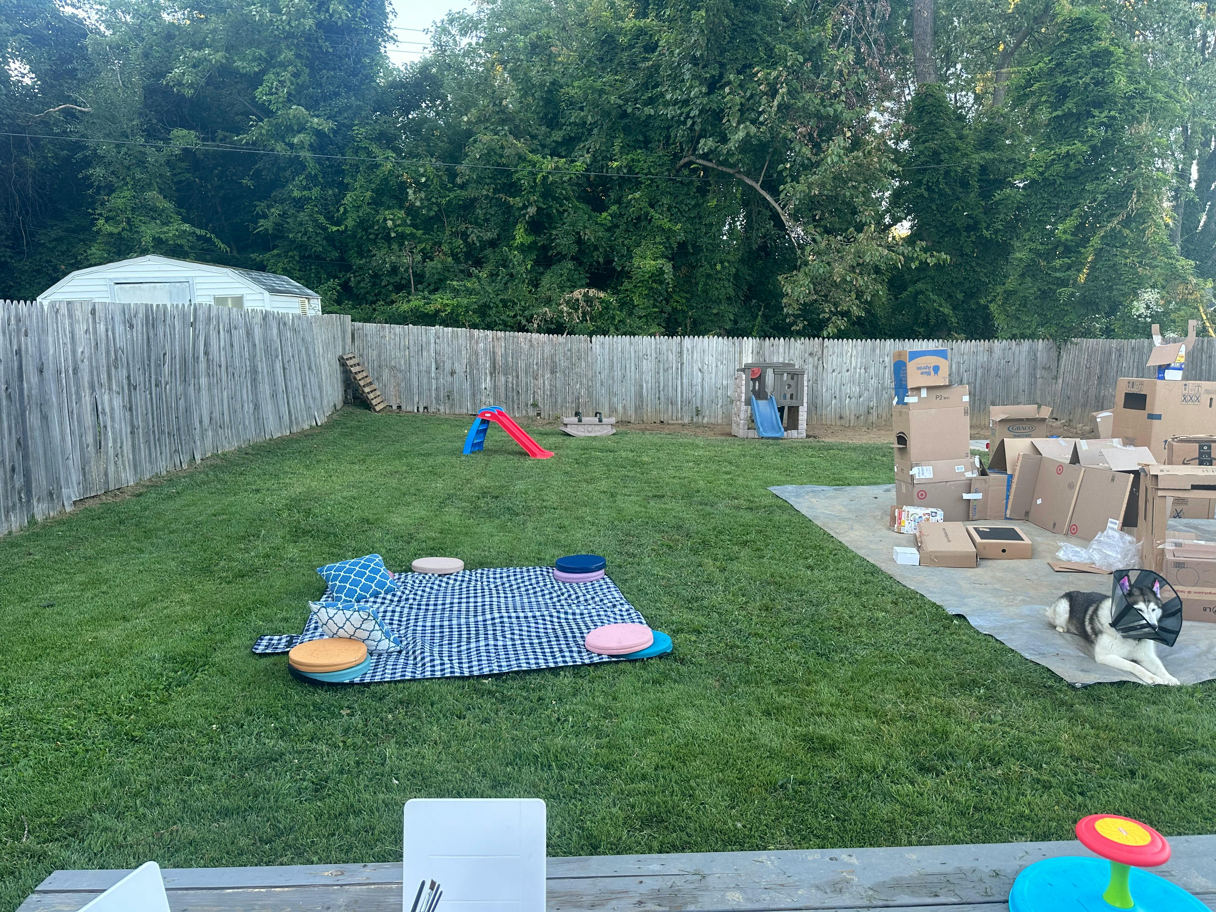 Backyard with a picnic blanket, small slide, and cardboard box structures