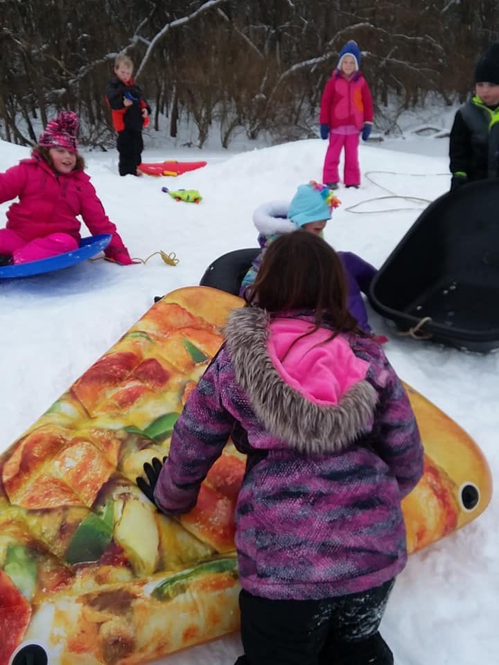 Children playing in snow with sleds and a pizza-shaped snow tube