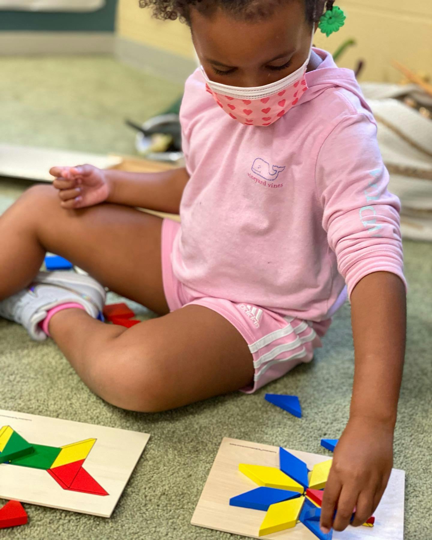 Child in a mask playing with colorful geometric puzzle pieces on the floor