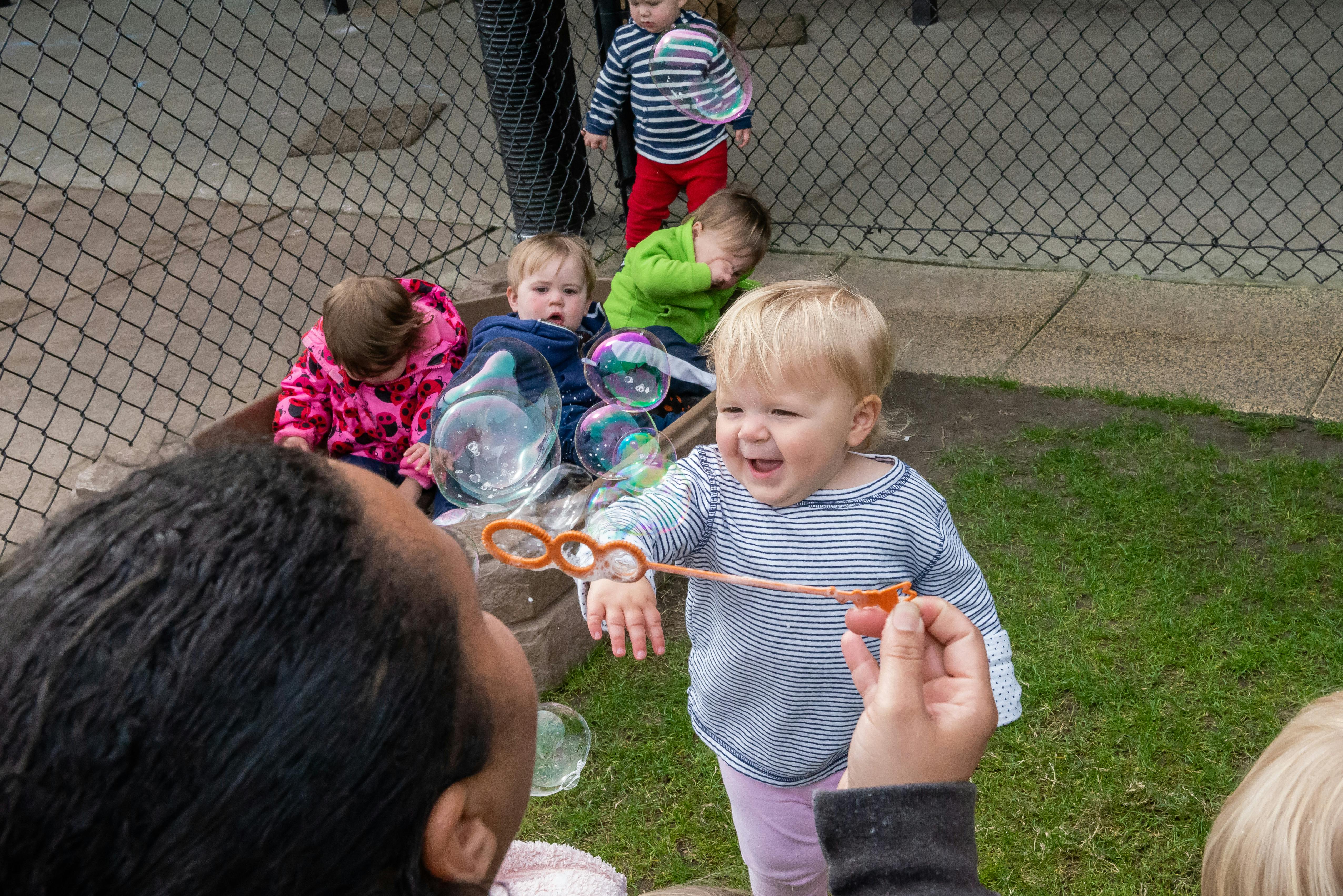 Person blowing bubbles for a child, other children in background