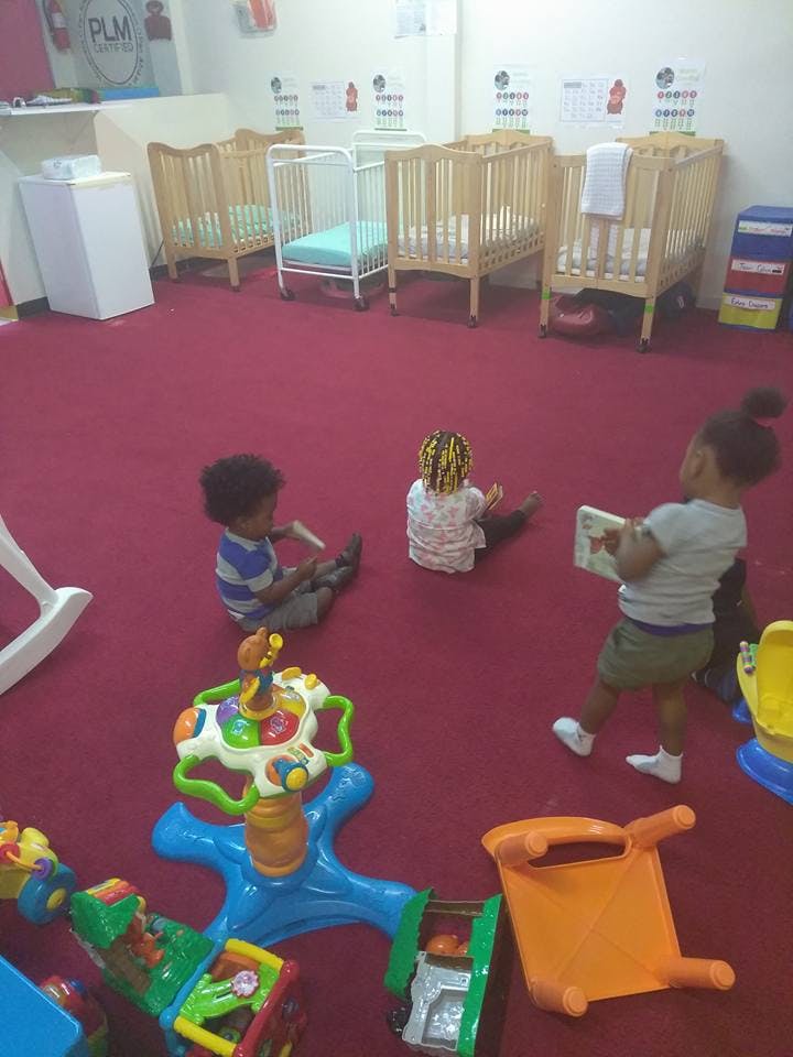 Three children playing on a red carpeted floor with toys and cribs in the background