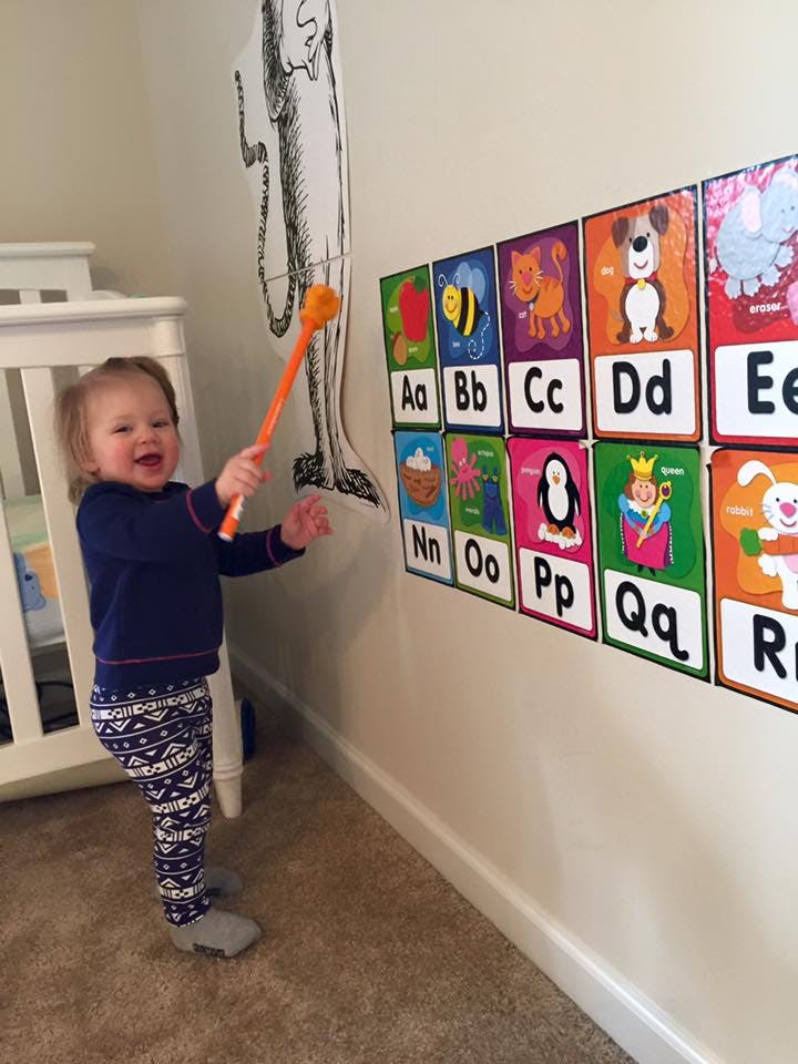 Child holding an orange stick near alphabet cards on a wall