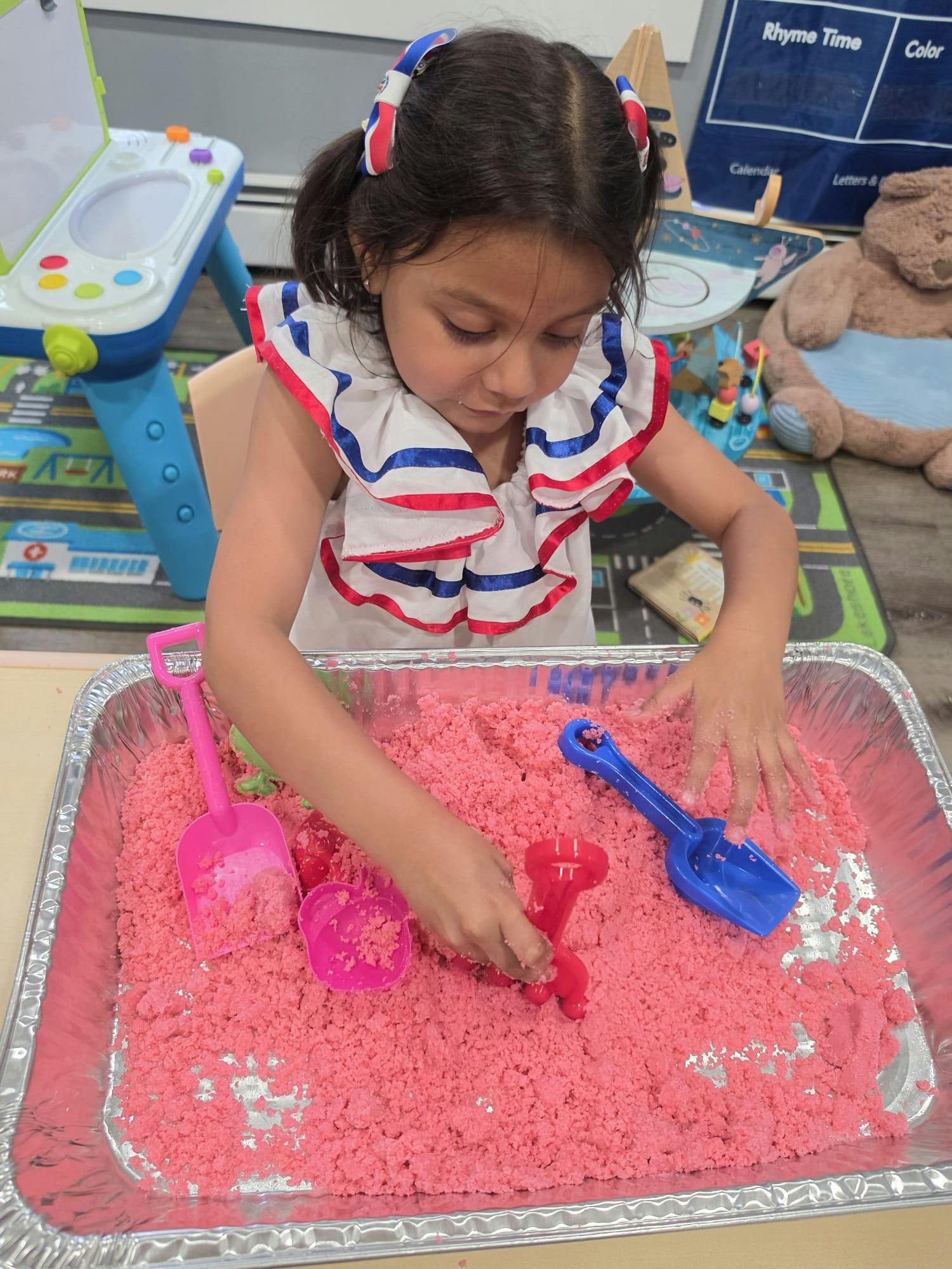 Child playing with pink kinetic sand in a metal tray with toy tools