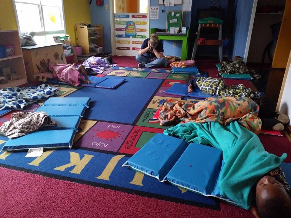 Person sitting on floor with children sleeping on mats in a classroom