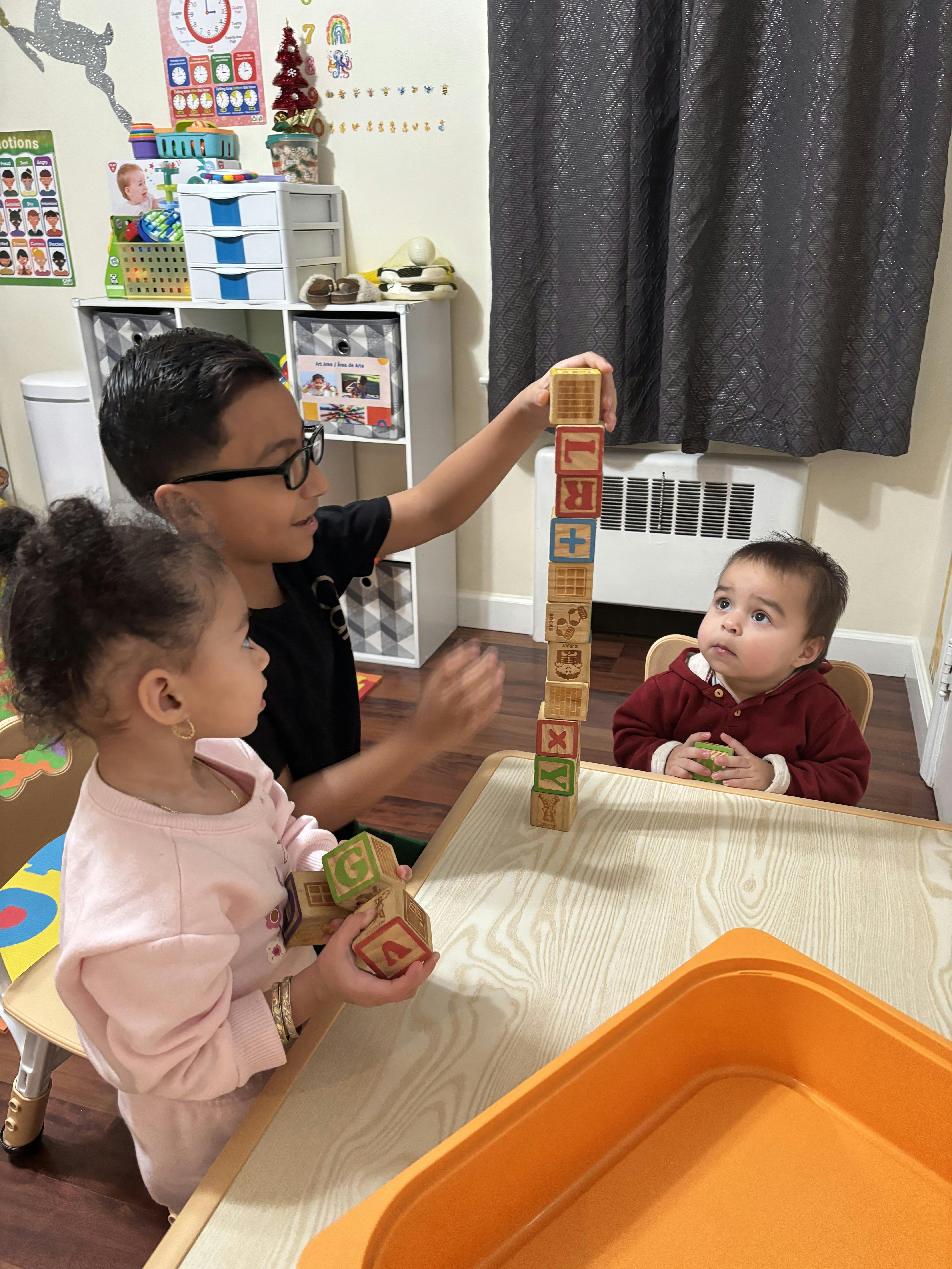 Child building block tower while two other children watch in a play area